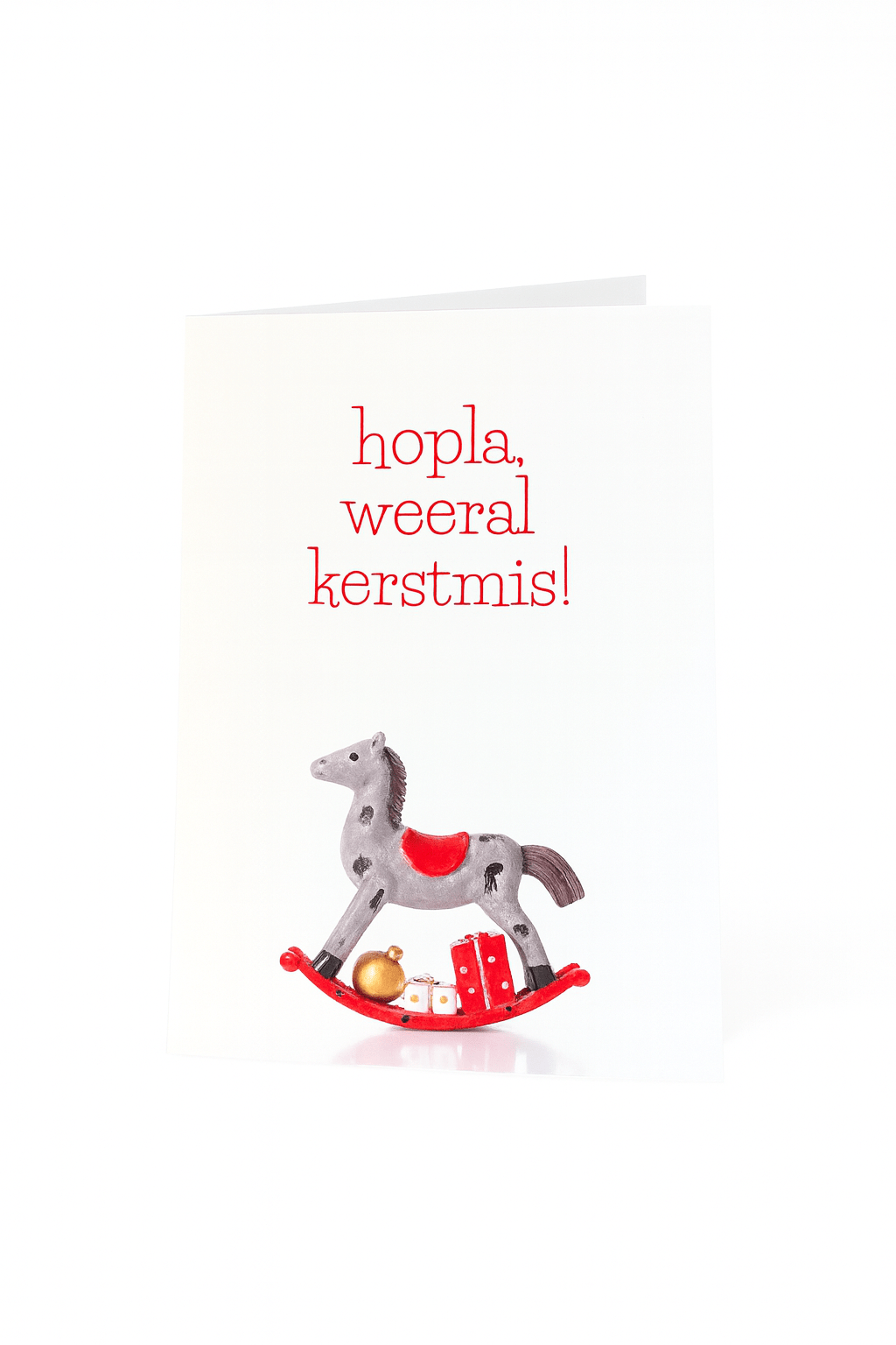 De Matriks Kerstkaart Hopla Weeral Kerstmis! van Matriks toont "hopla, weeral kerstmis!" boven een illustratie van een grijs-rood hobbelpaard met cadeautjes en een unieke kerstbal.
