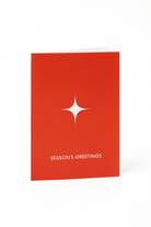 De Matriks Kerst- en Nieuwjaarskaart Season's Greetings van Matriks staat rechtop in rood, met een witte ster boven de vetgedrukte tekst "SEASON'S GREETINGS" en een strakke witte achtergrond voor een feestelijke, minimalistische look.
