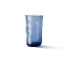 Een Paveau Swirl Longdrink Glas Midnight Blauw 46 cl, met een doorschijnende golvende textuur, staat op een wit oppervlak en werpt een vage schaduw naar rechts.