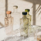 De Paveau Swirl Waterfles Moss Groen 0,75 l van Paveau, met golvend design en pastelgroene dop, staat samen met bijpassende borosilicaatglas tumblers zacht belicht op een zonovergoten witte ondergrond.