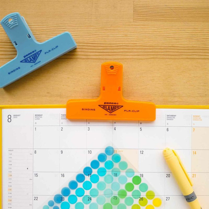 Oranje Penco PlaClip op een kalender, naast een lichtblauwe klem