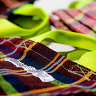 Close-up van de Puebco Check Document Tas van Puebco, met kleurrijk geruit ontwerp, fel geelgroene handgrepen, zichtbare stiksels en een wit label. De afbeelding benadrukt de unieke textuur en het patroon gemaakt van gerecyclede stoffen.