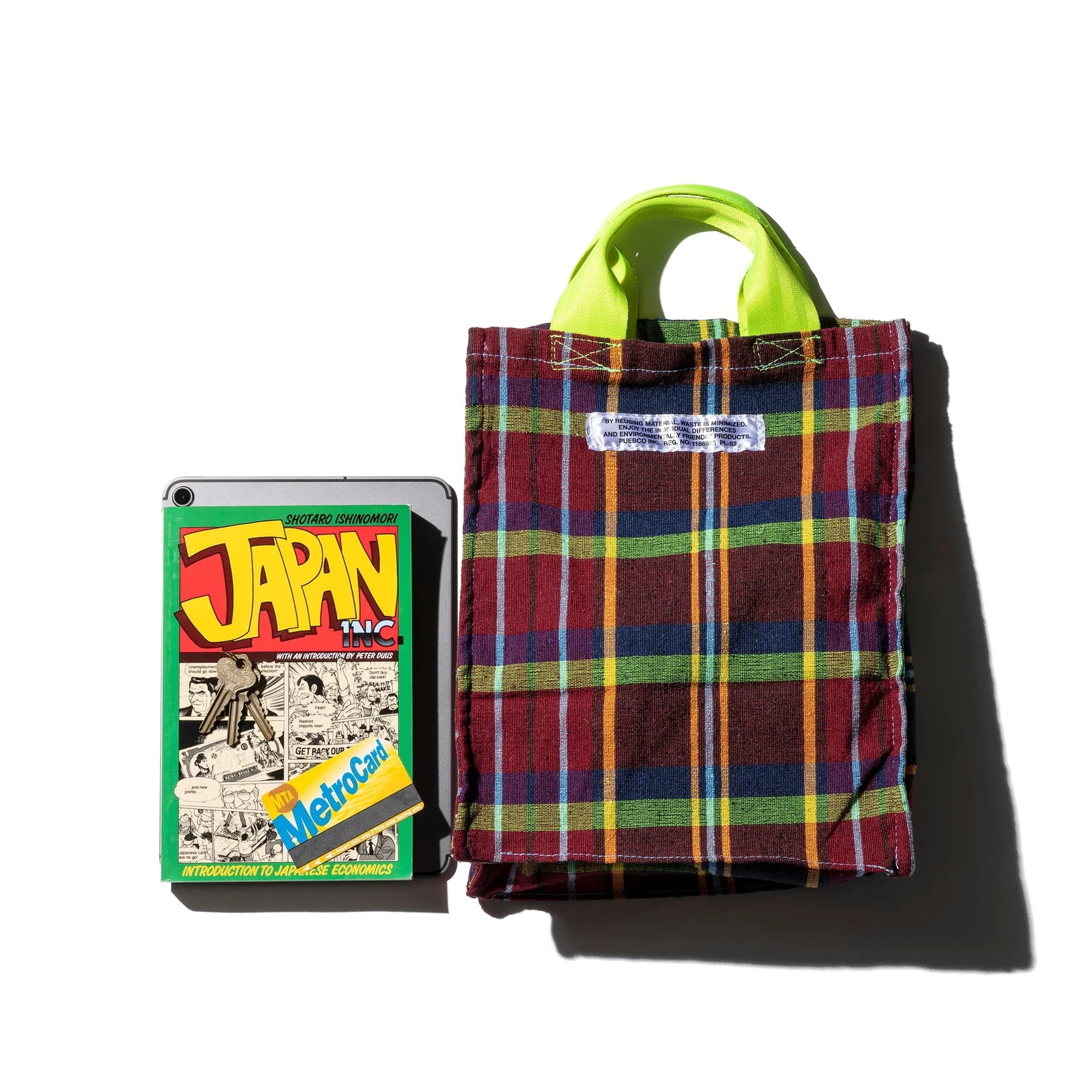 De Puebco Check Document Tas van gerecycleerd plaid met groene handvaten staat naast een tablet in een JAPAN INC.-hoes en deels onderliggende MetroCard, alles op een witte achtergrond. Ideaal als documententas.
