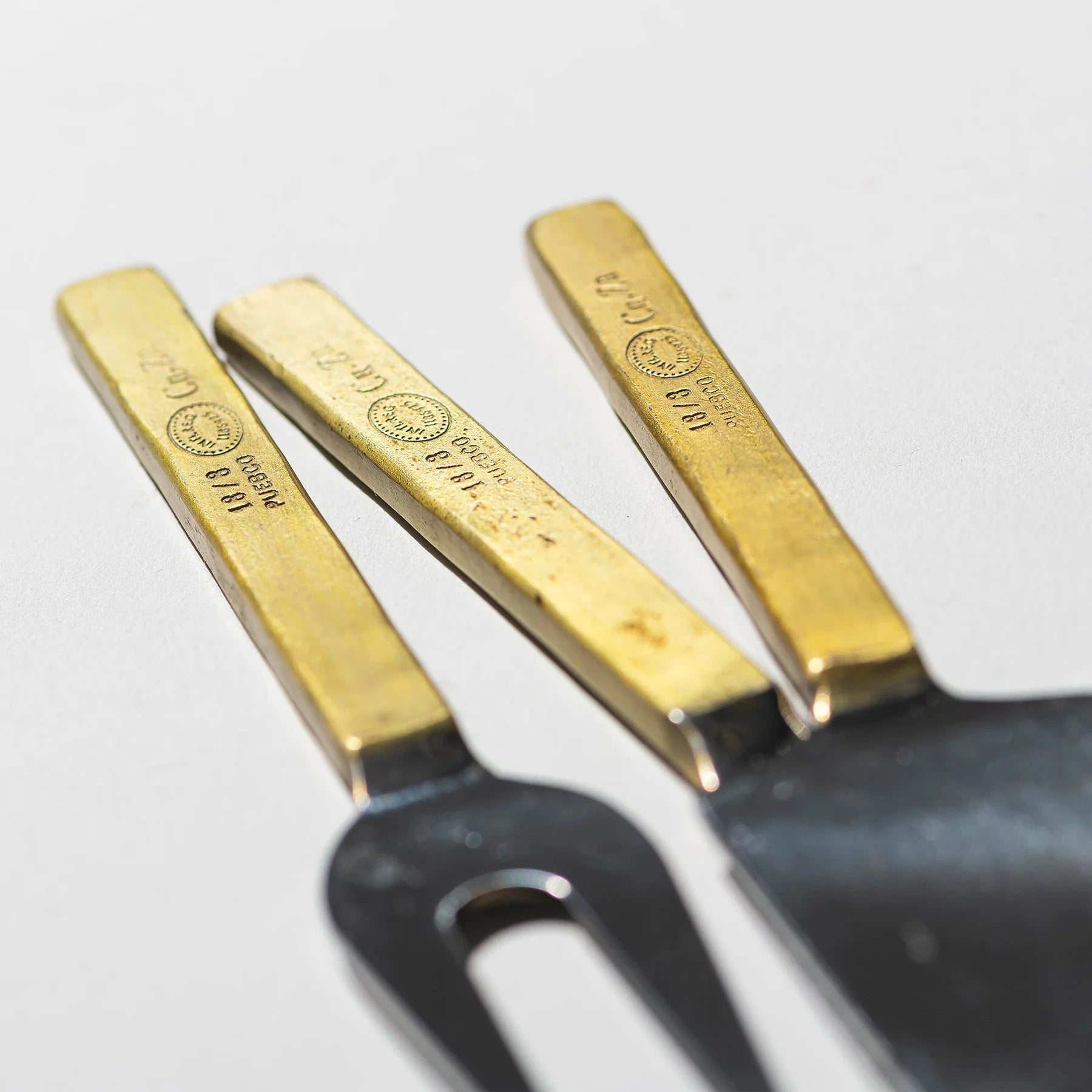 De Puebco Gegraveerde Kaasmesjes 3 st. van Puebco, met goudkleurige gegraveerde handvatten en roestvrijstalen uiteinden, zijn samengebracht op een wit oppervlak met de tekst en logo's duidelijk zichtbaar op de elegante handvatten.