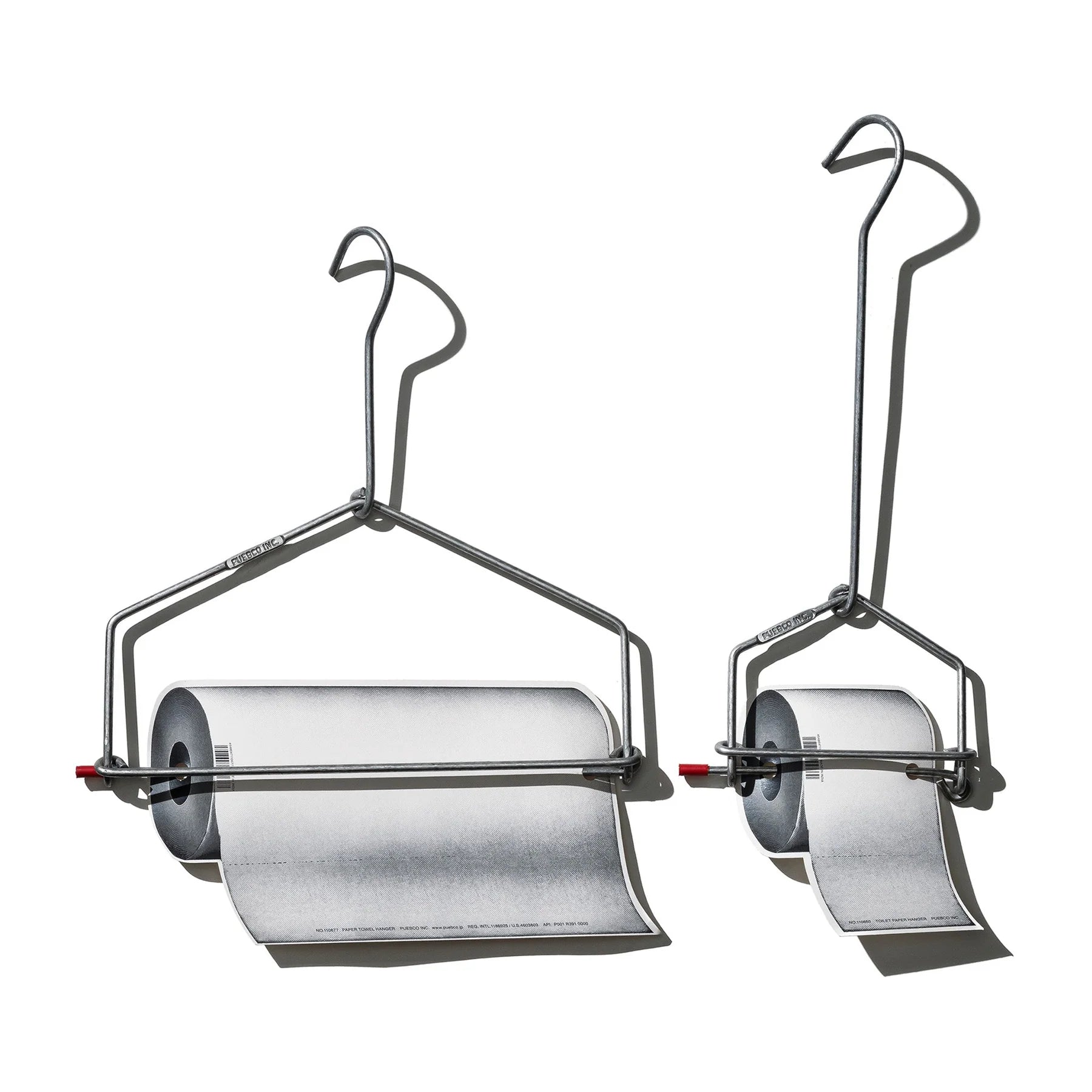 Twee metalen Puebco Keukenrolhouderhangers houden elk een papierrol vast die naar beneden rolt tegen een witte achtergrond, met sterke schaduwen naar rechts.