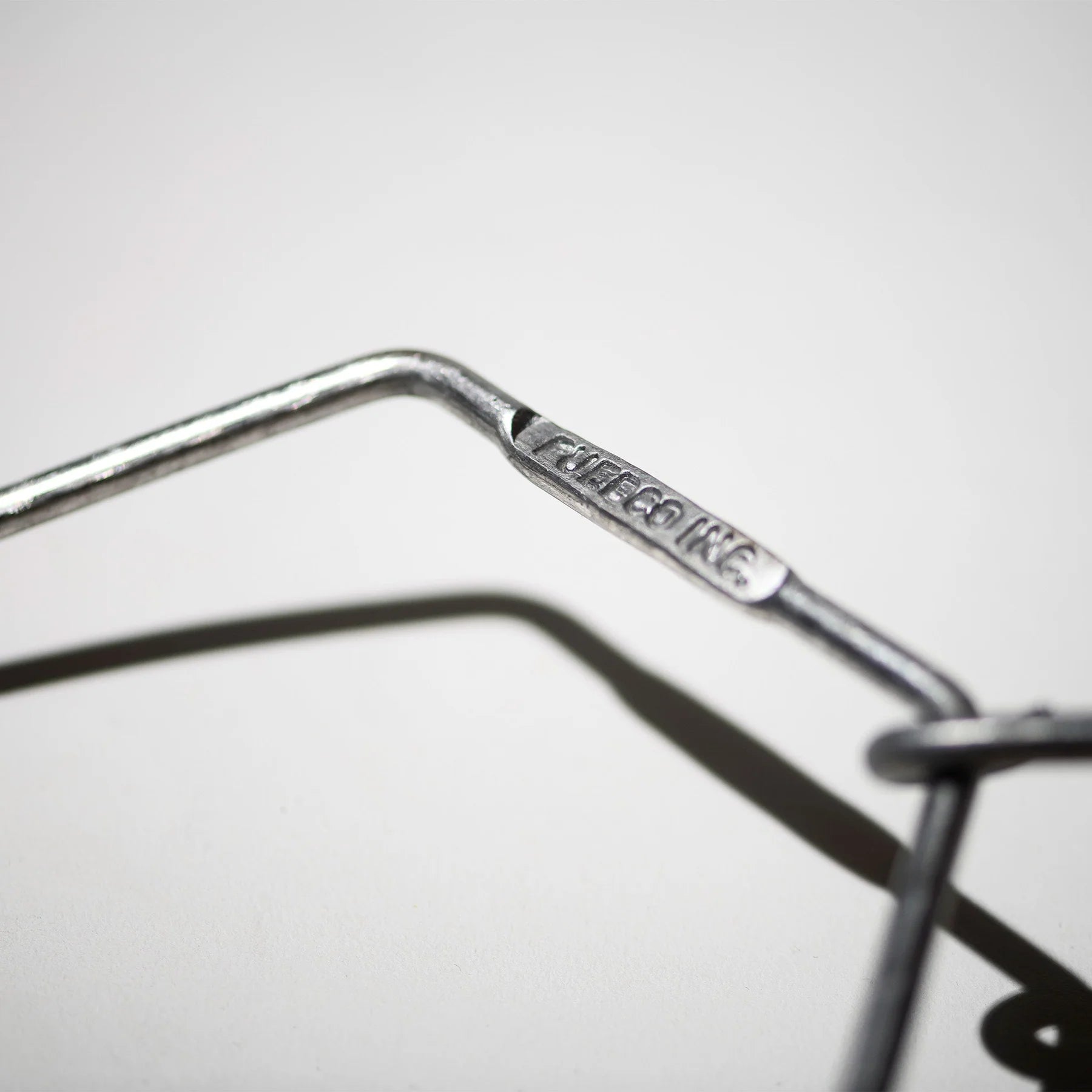 Close-up van een metalen Puebco Keukenrolhouder Hanger, met "CHEEGO INC." erop gegraveerd. De scherpe focus benadrukt de gravure, terwijl de achtergrond wazig lijkt. Merk: Puebco.