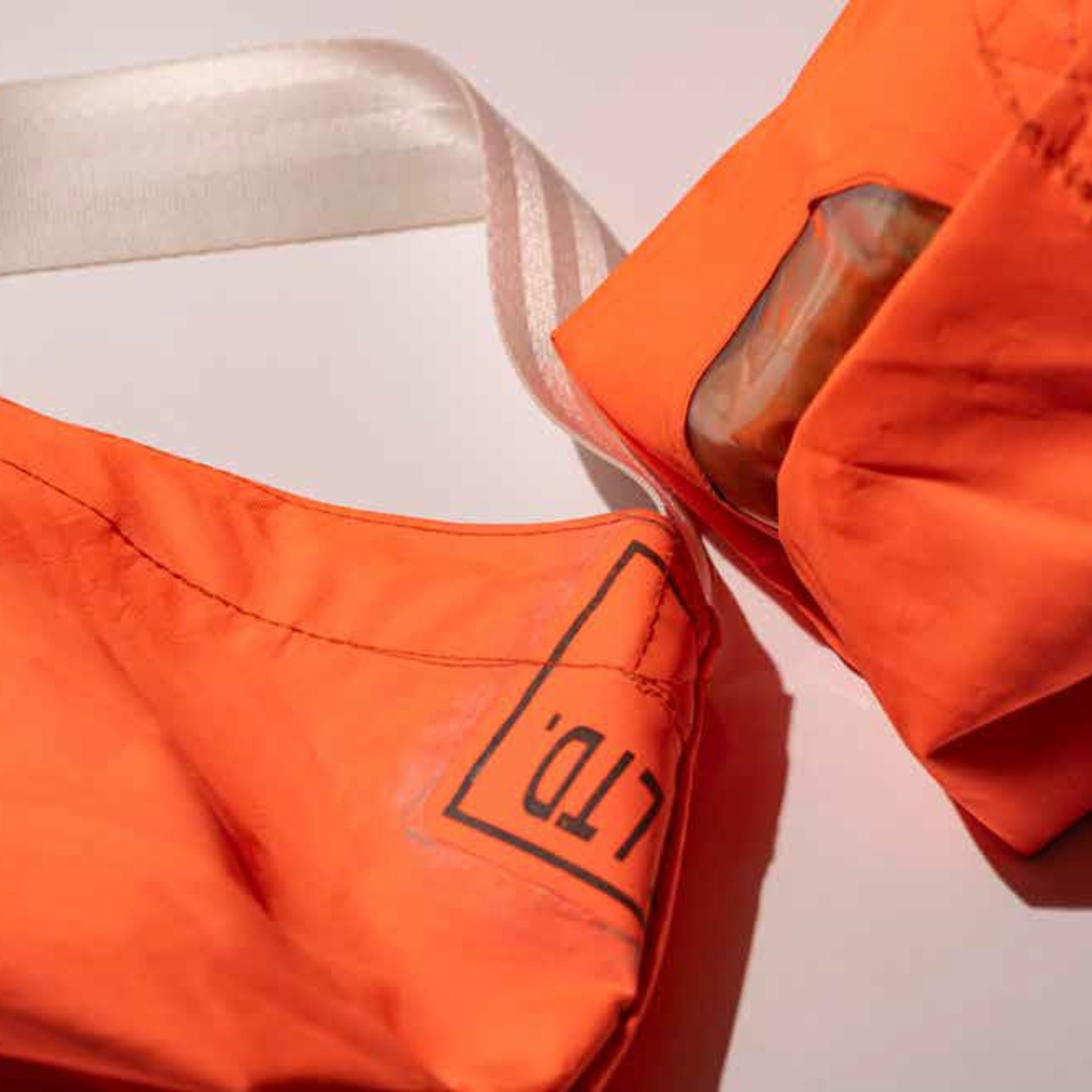 Er worden twee oranje Puebco Limited Edition Vintage Emergency Boat Tassen van gerecupereerd bootmateriaal getoond. De ene heeft een doorzichtig vak met een voorwerp erin, op de andere staat "LTD" in zwarte tekst. Beide liggen op een licht oppervlak.