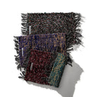 Drie veelkleurige geweven sjaals met textuur en franjes zijn diagonaal gerangschikt op een witte achtergrond, elk met een uniek patroon. Hun ambachtelijke stijl doet denken aan de Puebco Mat Gerecycleerd Textiel 63/41 van Puebco. Schaduwen naar rechts.