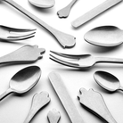 Allerlei zilverwerk, waaronder de Serax Merci Bestek 24-delig set, is in een cirkel gerangschikt op een wit oppervlak, waarbij sommige gebruiksvoorwerpen aan de uiteinden zijn voorzien van speelse handgevormde ontwerpen.