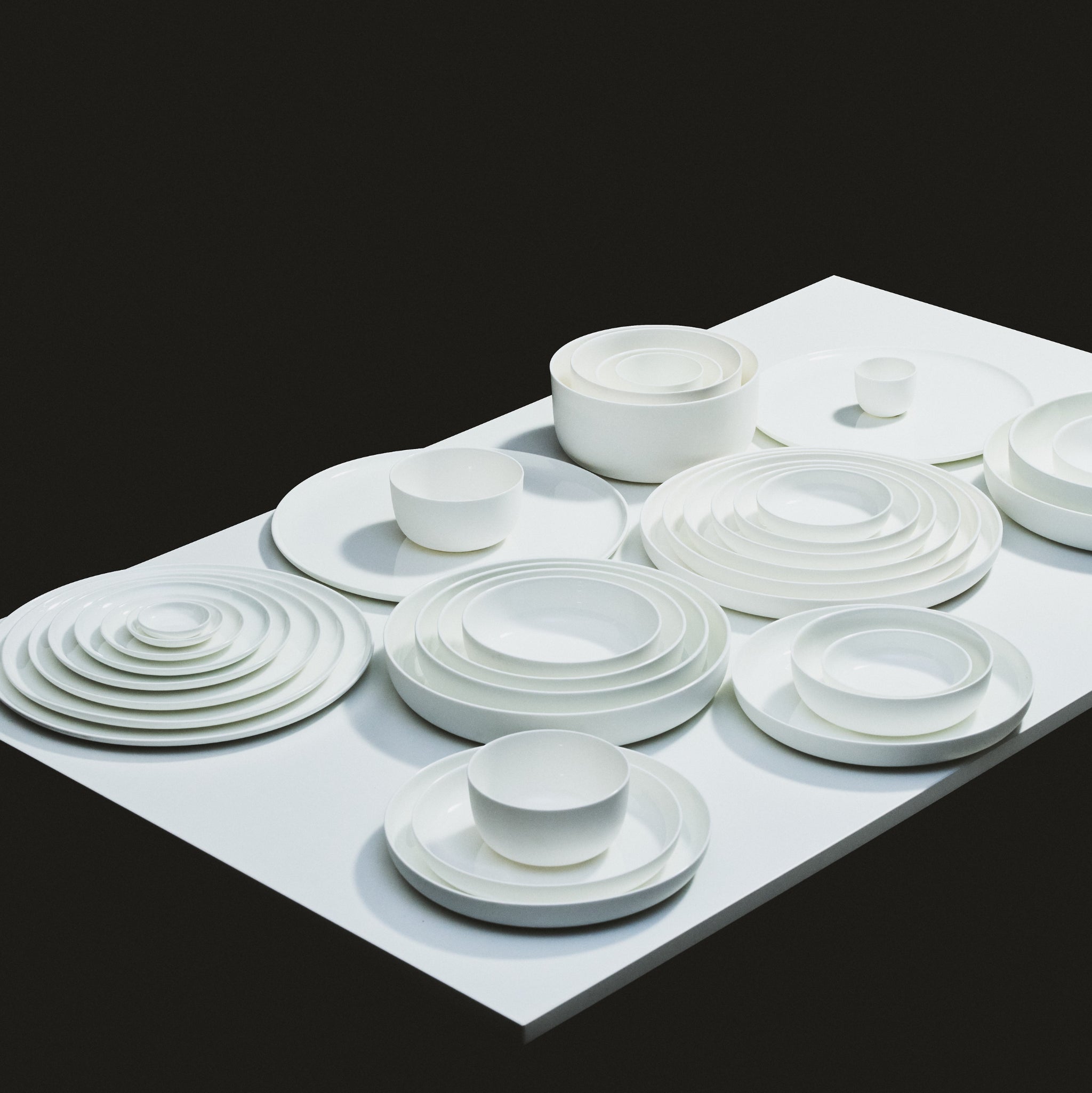 Op een witte tafel staan stapels Serax Base Diep Bord D16 borden - elegant wit keramisch servies van Serax - gerangschikt in concentrische cirkels tegen een zwarte achtergrond, wat qua ontwerp doet denken aan het klassieke Chinees porselein.
