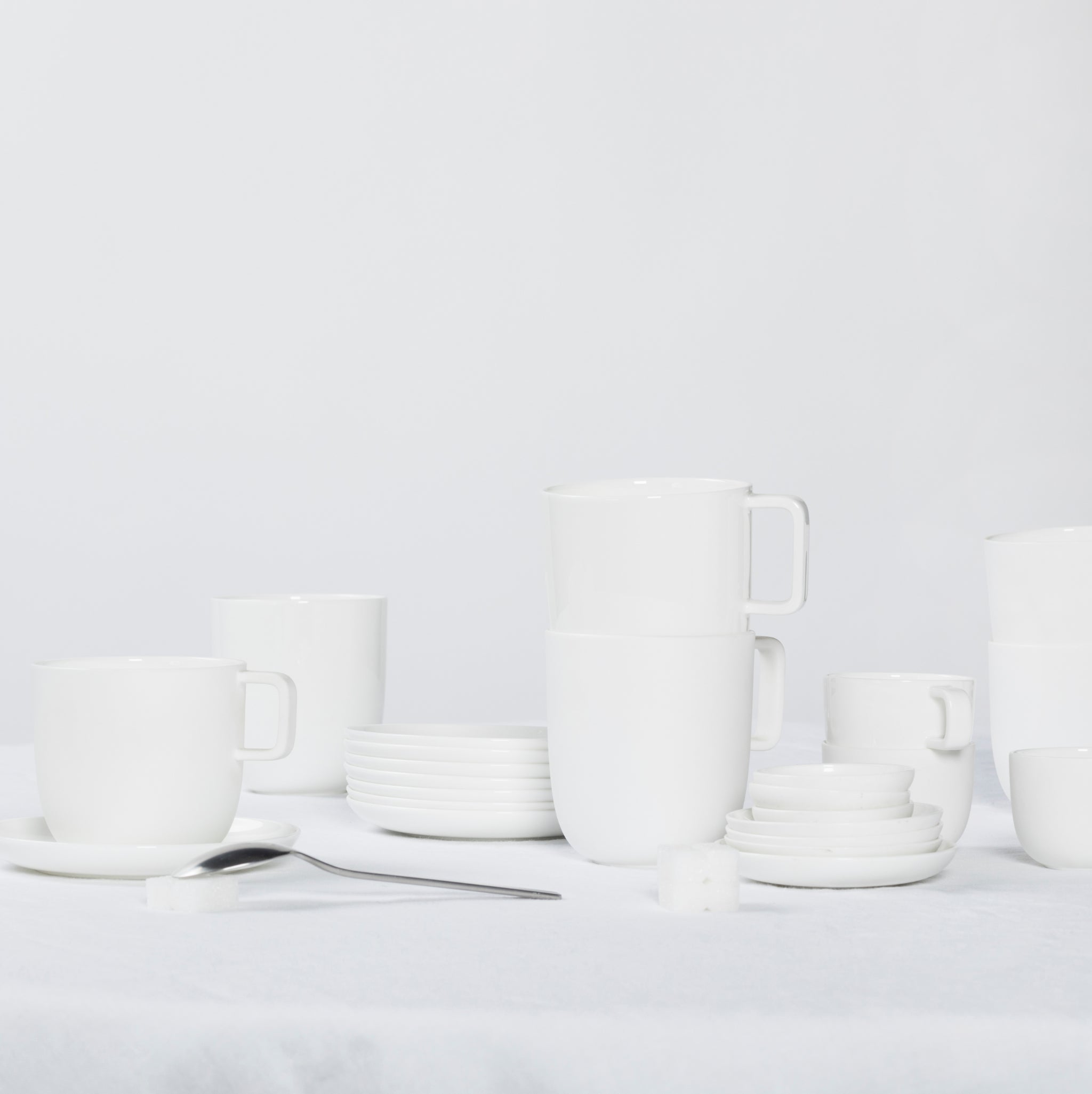 De Serax Base Koffiekop zonder Oor 30 cl, van Serax, staat op een strak wit oppervlak met minimalistische accenten - een metalen lepel en suikerklontjes - en creëert een sereen tafereel geïnspireerd op Chinees porselein.