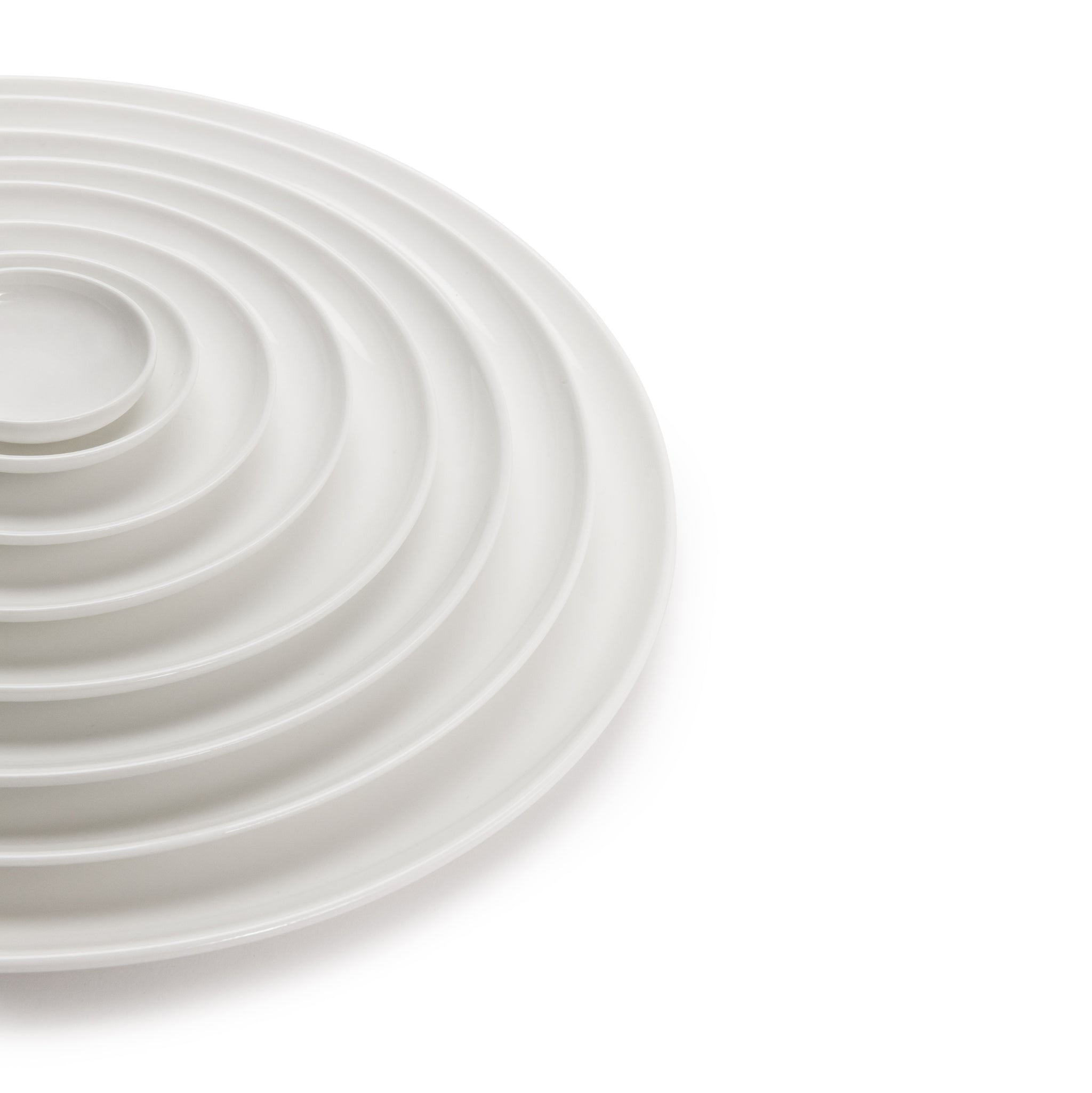 Een set witte, ronde borden van Serax Base Laag Bord D12, concentrisch gerangschikt in oplopende grootte op een witte achtergrond, die een nestachtig patroon vormen, waarbij een deel van de rangschikking is uitgesneden. Ontworpen door Studio Piet Boon.