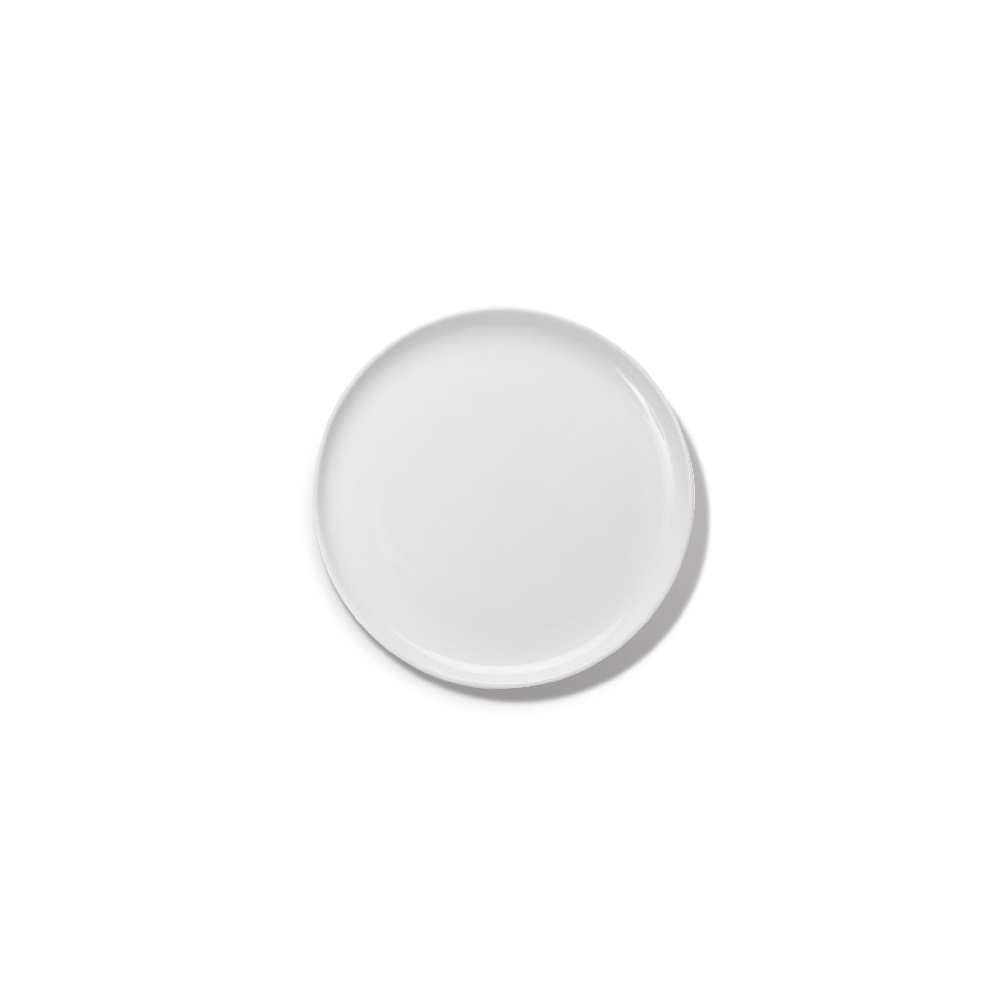 De Serax Base Laag Bord D20, een eenvoudig rond bord van wit keramiek van Serax, is gecentreerd op een witte achtergrond, werpt een zachte schaduw naar rechts en doet denken aan de verfijnde eenvoud van Chinees porselein.