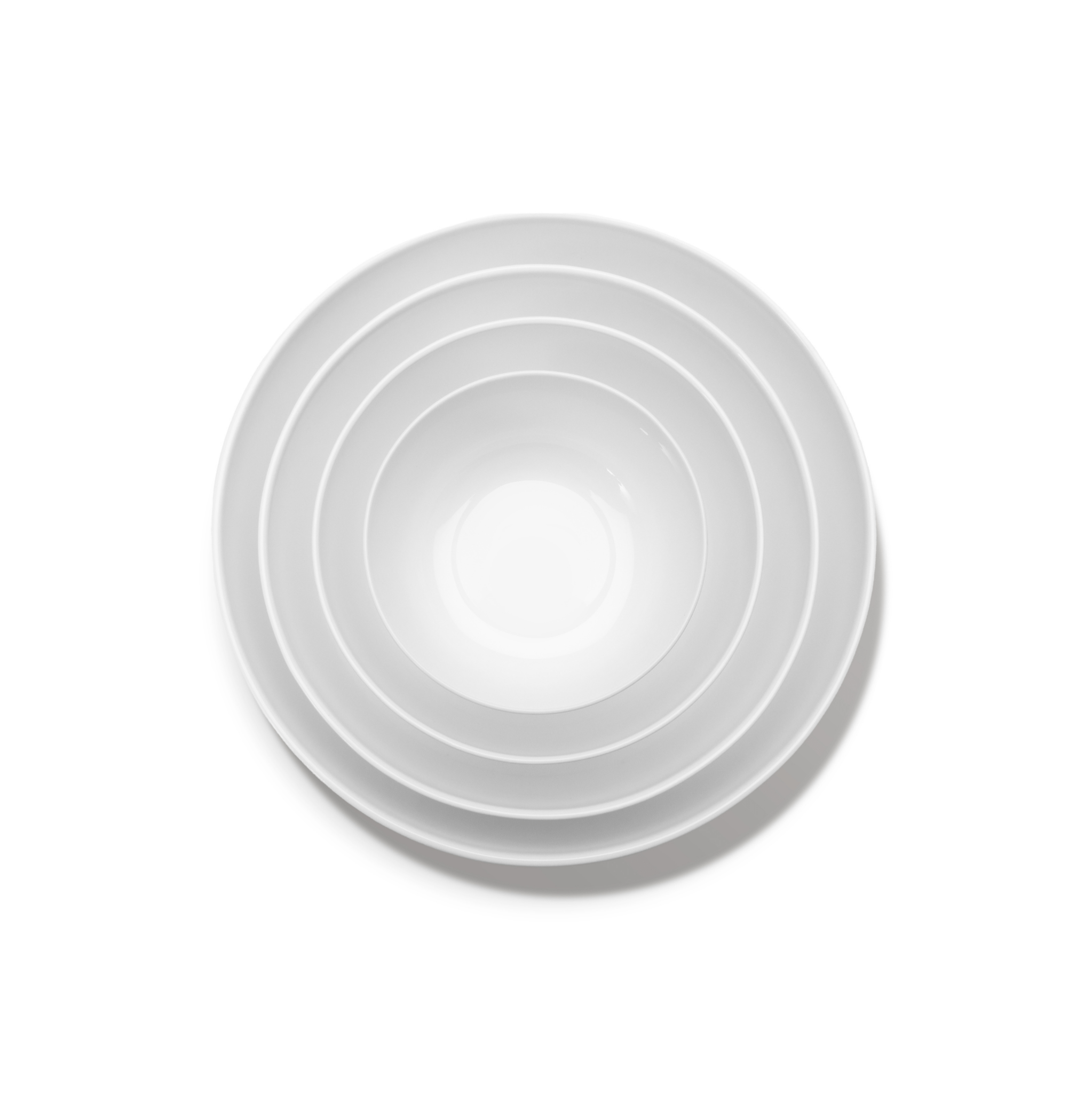 Vier witte, ronde Serax Base Lage Kom D20 porseleinen kommen van Serax van verschillende grootte nestelen zich in elkaar, van bovenaf gezien op een effen witte achtergrond.