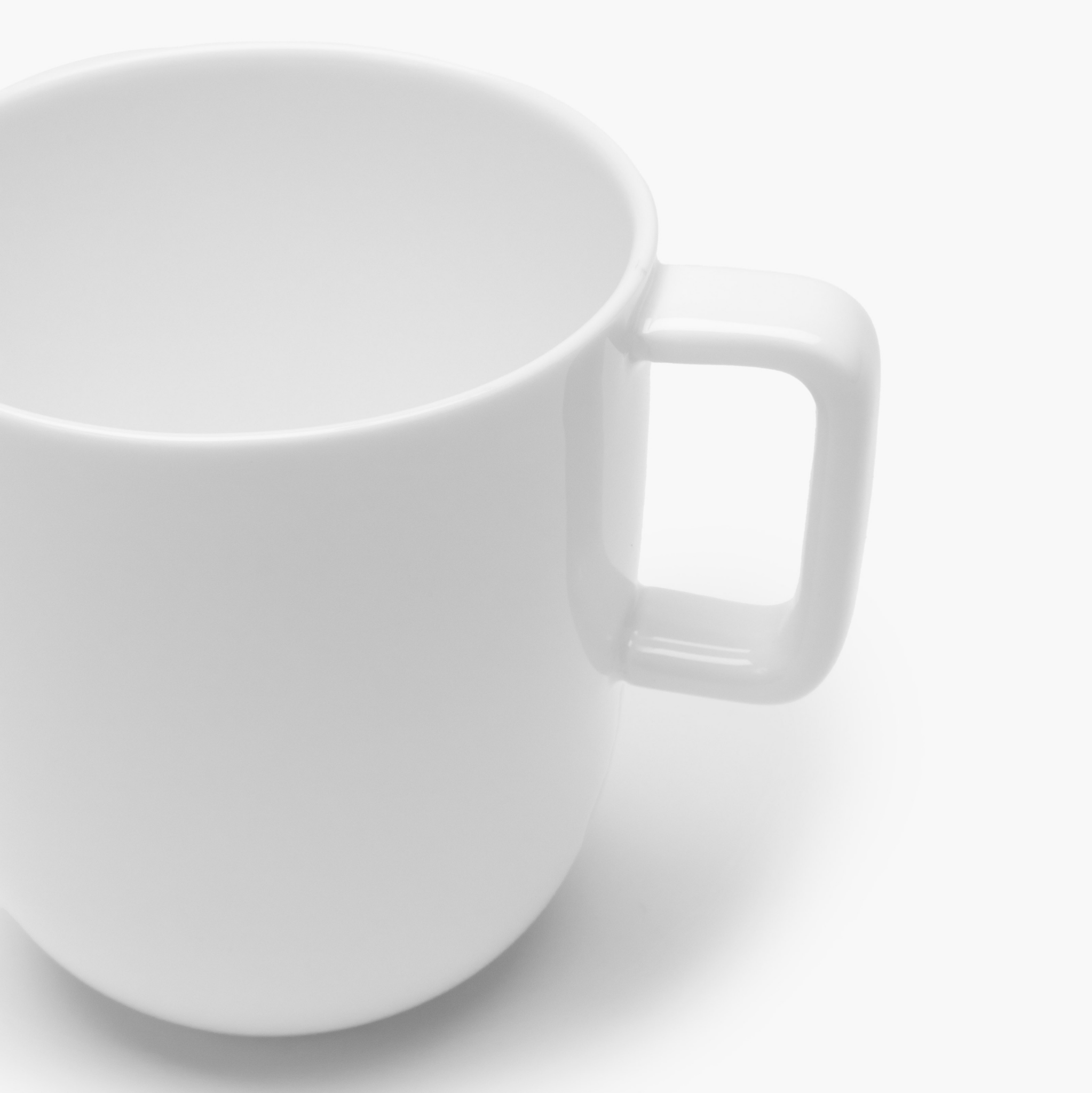 Een Serax Basis Theekop met Oor 35 cl van Serax, gefotografeerd op een witte achtergrond. De foto toont slechts een deel van de witte mok, met de nadruk op de linkerbovenkant en het handvat.