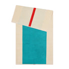 De Suite 702 Badhanddoek Rood Turquoise 70/140 van Suite 702 is een beige handdoek van biologisch katoen, met een turquoise rechthoek en een rode streep aan de bovenkant, gevouwen om het op Karel Martens geïnspireerde ontwerp te benadrukken.