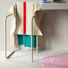 Een modern handdoekenrek houdt een Suite 702 Badhanddoek Rood Turquoise 70/140 vast. Opgevouwen handdoeken rusten op een zwevende plank en een roze badmat bedekt de lichte tegelvloer, waardoor een strakke, minimalistische look ontstaat.