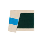 De Suite 702 Badmat Aqua Donkergroen 50/80, gemaakt van biologisch katoen, heeft een donkergroene rechthoek met een beige rand en is hier gecombineerd met een bijpassende beige handdoek met een opvallende blauwe streep, beide geïnspireerd door Karel Martens.