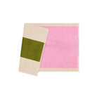 De Suite 702 Badmat Roze Olijfgroen 50/80, een rechthoekige roze badmat van biologisch katoen met een beige rand, wordt getoond naast een gevouwen beige handdoek met een brede olijfgroene streep, beide uit Suite 702, weergegeven op een witte achtergrond.