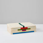 Een set van drie crèmekleurige Suite 702 Gastendoekjes (Set D 30/50) gemaakt van biologisch katoen, elk met minimale kleurrijke geometrische lijnen geïnspireerd door Karel Martens, weergegeven op een wit oppervlak en een lichtgrijze achtergrond.