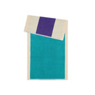 Het Suite 702 Handdoek Turquoise Paars 50/100 is een rechthoekig biologisch katoenen handdoek met een groenblauw hart, crèmekleurige randen en een opvallende paarse streep langs de gevouwen rand - een artistiek badkamertextiel van Suite 702 op een witte achtergrond.