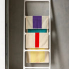 Drie Suite 702 Handdoeken Rood Geel 50/100 hangen op een wit rek tegen een grijze muur, met gedurfde, op Karel Martens geïnspireerde strepen in levendig rood en geel. Gemaakt van biologisch katoen.