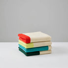 Een stapel van vier Suite 702 Handdoeken Rood Geel 50/100, elk met een andere gekleurde rand, ligt gevouwen op een wit oppervlak met een lichtgrijze achtergrond. Geïnspireerd door Karel Martens en gemaakt van biologisch katoen.