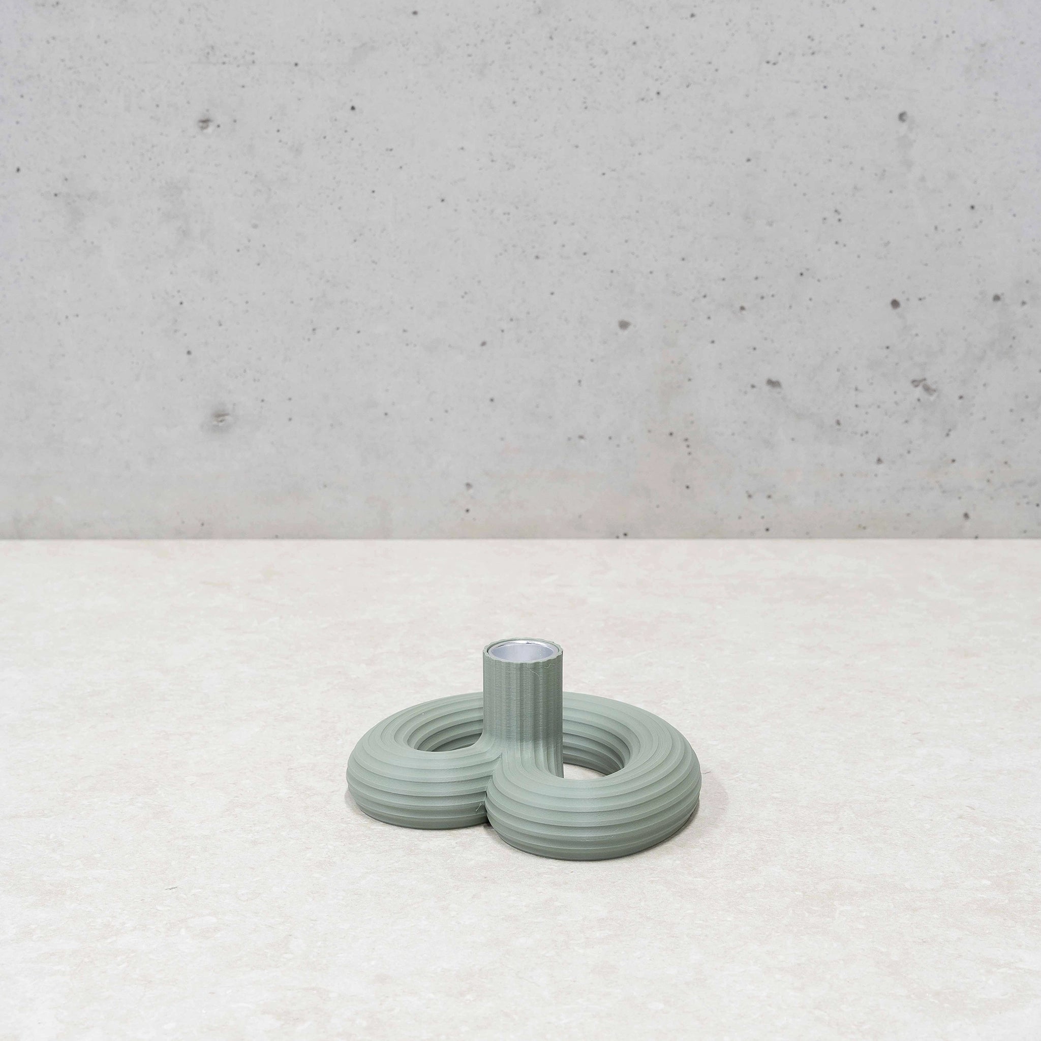 De Wavy Kandelaar Muntgroen van Wavy Design Studio, een minimalistische golvende kandelaar, staat op een lichtgekleurd oppervlak naast een lichtgroene ronde vaas met geribbelde textuur, tegen een betonnen muur.