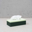 De Wavy Tissuebox Highland Groen/Munt van Wavy Design Studio staat op een lichte ondergrond met een wit tissue dat uit de lichtgroene deksel steekt. Op de achtergrond is een effen, lichtgrijze muur zichtbaar.