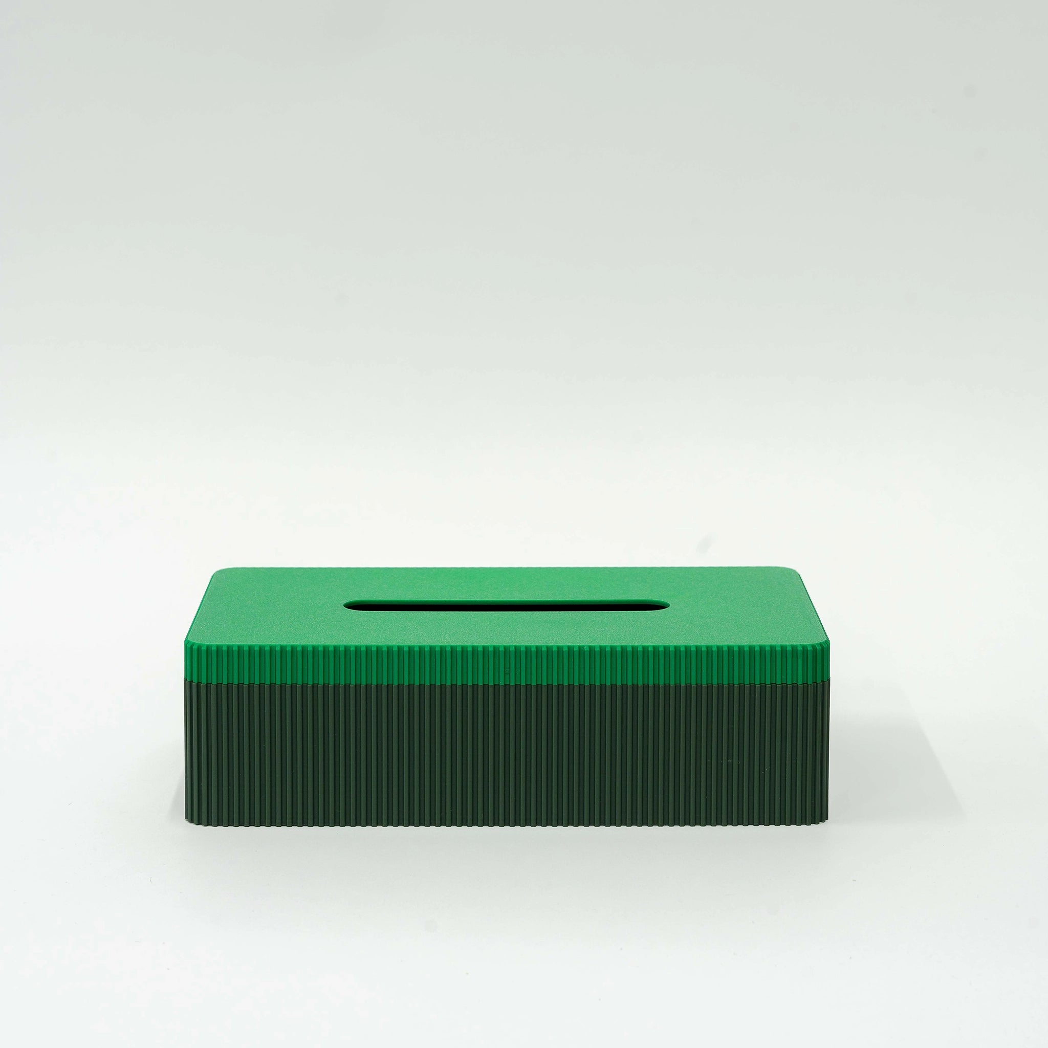 De Wavy Tissuebox Highland/Pearl Groen van Wavy Design Studio is een rechthoekige, groene, geribbelde tissuebox met een horizontale gleuf aan de bovenkant, gemaakt van gerecycled hout voor een duurzaam ontwerp, afgebeeld tegen een effen witte achtergrond.