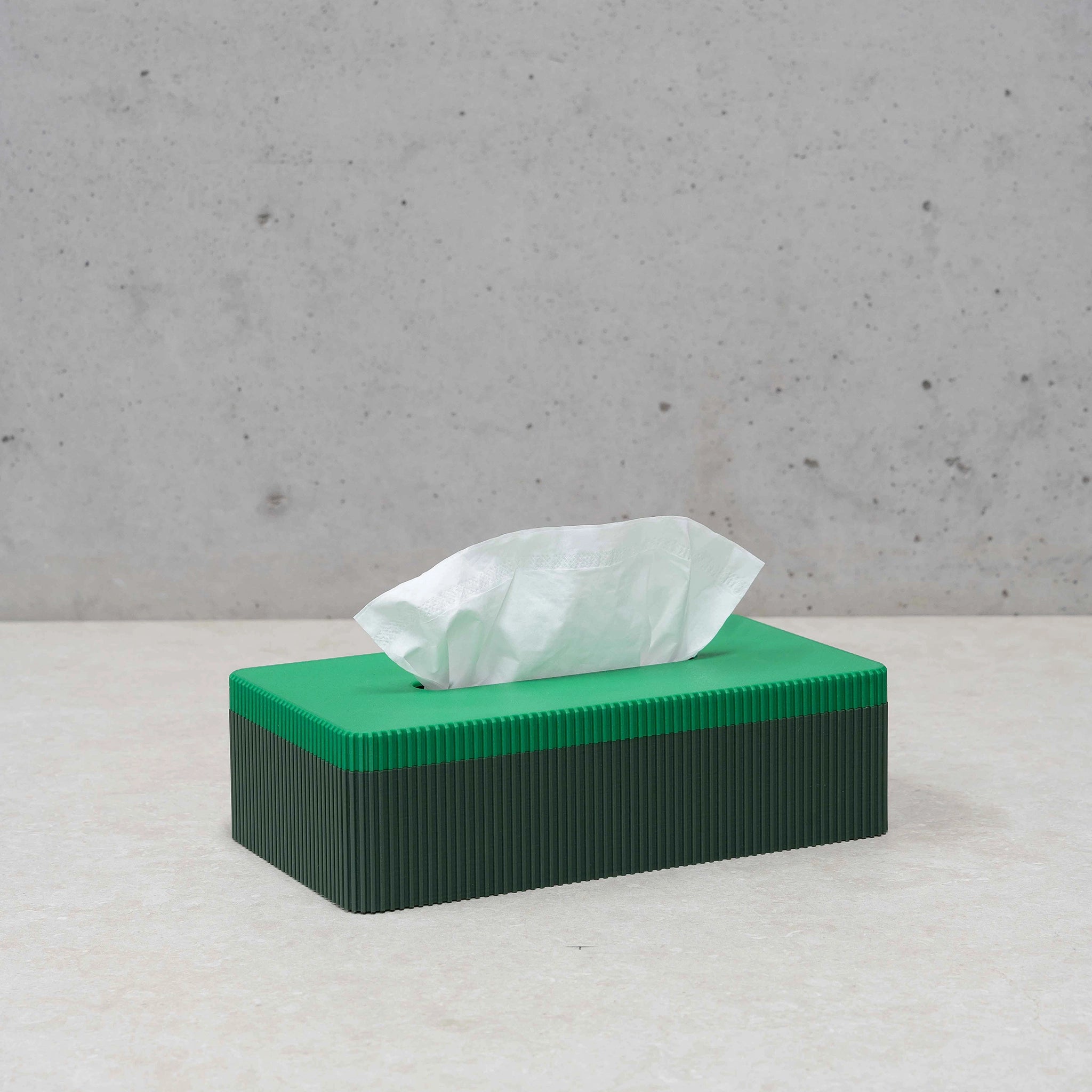 De Wavy Tissuebox Highland/Pearl Groen van Wavy Design Studio is een groene rechthoekige tissuebox gemaakt van gerecycleerd hout, voorzien van een enkele witte tissue en ideaal voor liefhebbers van duurzaam design.