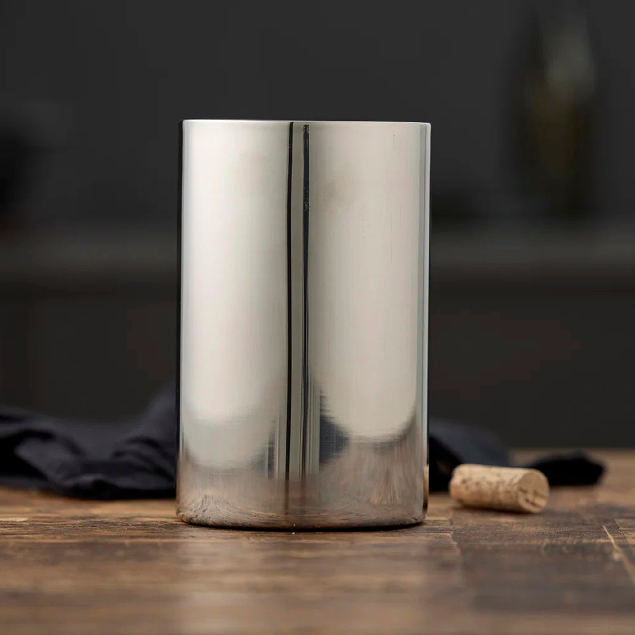 De Zone Denmark Funktion-wijnkoeler van Hay, met een dubbelwandige roestvrijstalen constructie, staat rechtop op een houten tafel, met een kurk en een zwart doek op de achtergrond.