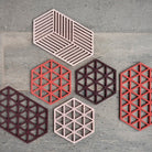 Zes Zone Denmark Triangles Trivet Kalamata siliconen onderzetters in roze, rood en bordeaux zijn gerangschikt op een grijs stenen oppervlak. Elke Zone Denmark onderzetter heeft een uniek zeshoekig ontwerp met geometrische uitgesneden patronen.