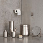 De Zone Denmark Ume Tandenborstelhouder Staal en andere roestvrijstalen badkameraccessoires van Zone Denmark staan uitgestald op een grijs aanrechtblad, met daarboven een wc-papierrol.