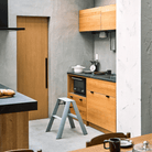 Moderne keuken met lichthouten kastjes, betonnen muren en een Hasegawa Lucano Ladder 2 Step Dusty Mint op de vloer. Op het aanrecht staan een digitale weegschaal, een wit bord en keukengerei. De magnetron is ingebouwd en weerspiegelt de Japanse design flair.