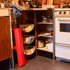 Gezellige keukenhoek met open planken voor potten en schalen. Een wit fornuis staat naast een drielaags fruitmand met bananen en appels. De rode Hasegawa Lucano Ladder 2 Step van Hasegawa leunt vlakbij en voegt charme toe aan de ruimte.