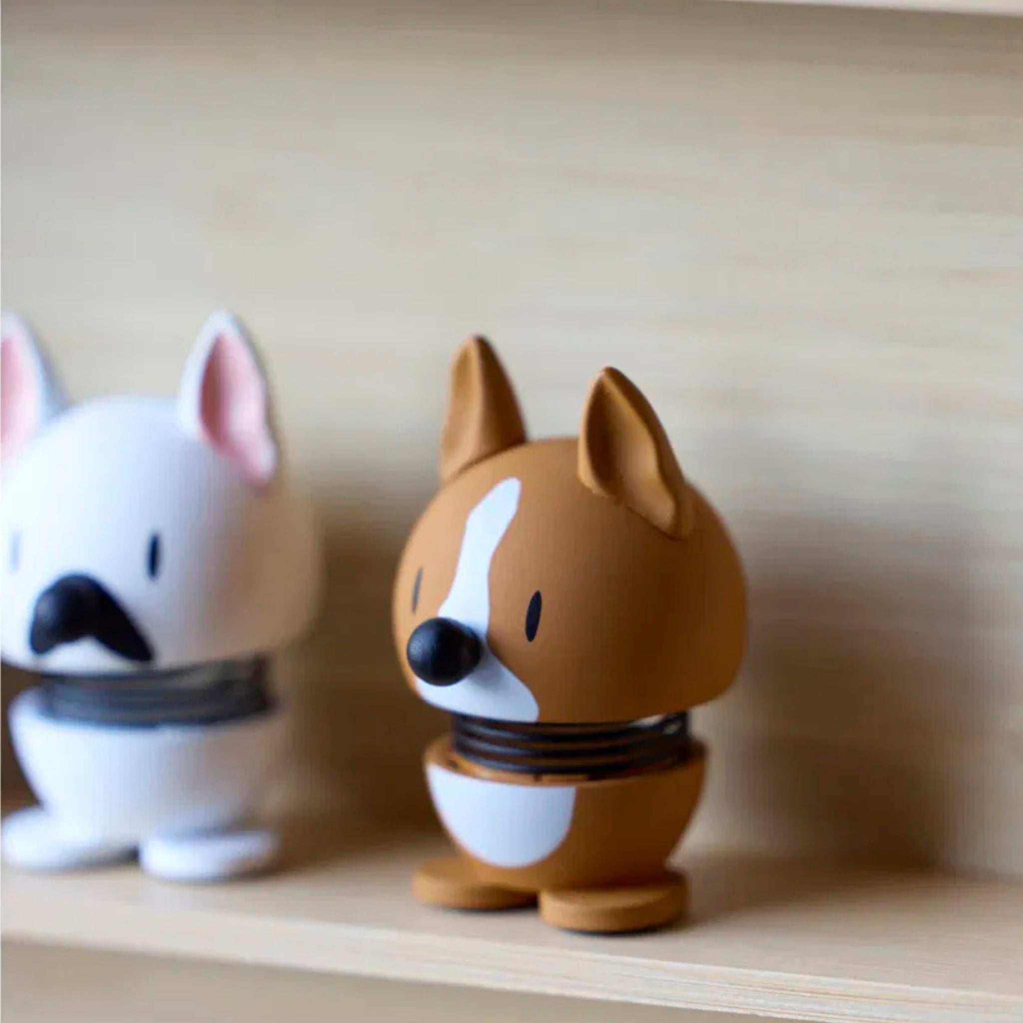 Twee Hoptimist Franse Bulldog Hond Wit/Zwart XS figuurtjes met verende lijfjes zitten op een houten plank - één bruin met een witte streep, één wit/zwart. Hun speelse uiterlijk maakt ze het perfecte cadeau voor hondenliefhebbers.