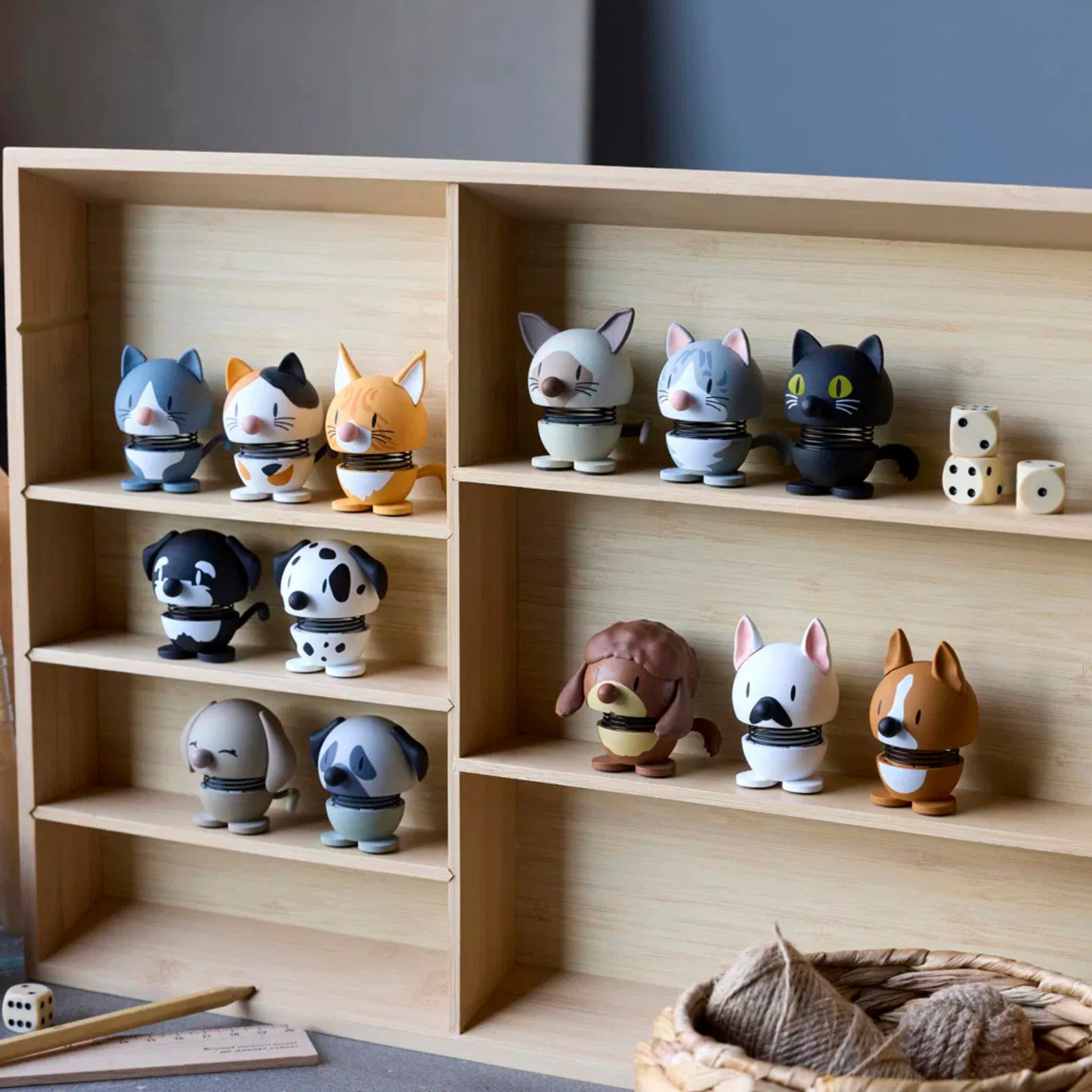 Op een houten plank staan kleine, ronde dierenfiguurtjes, waaronder katten, honden, een schaap en het Hoptimist Tijgerkat Oranje XS van Hoptimist - een ideale oranje decoratie of cadeau voor kattenliefhebbers. Dobbelstenen en garen rusten op de tafel vooraan.