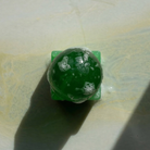 Een ronde, groene Matias Moellenbach OBA-zeep met aloë vera en wat belletjes ligt op een vierkant, groen zeepbakje en werpt een schaduw op een licht, licht gestructureerd oppervlak.