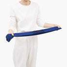 Een persoon in een witte outfit houdt een Shupatto Opvouwbare Boodschappentas Mori Groen M in beide handen tegen een effen witte achtergrond. Dit toont het compacte, gestructureerde ontwerp van deze rechthoekige Shupatto tas.