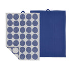 Er worden twee rechthoekige Södahl Bubbles Theedoek Blauw (2 st.) theedoeken getoond: een effen blauwe, de andere lichtgrijs met grote blauwe cirkels in een Scandinavisch dessin. Beide hebben een blauwe ophanglus aan de bovenkant.