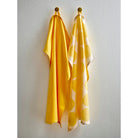 Twee gele handdoeken-Södahl Bubbles Theedoek Geel 2 st. - hangen aan wandhaken; de ene is effen, de andere toont grote gele cirkels op wit en brengt een Scandinavisch tintje in je keuken.