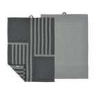 Set van twee Södahl Reflection Theedoek Ash: een effen lichtgrijze, de andere donkergrijs met lichtgrijze strepen in een geometrisch Scandinavisch patroon. Beide hebben ophanglussen; de gestreepte handdoek is gedeeltelijk gevouwen aan één hoek.