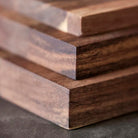 Close-up van de hoeken van drie gestapelde Tareq Taylor Tarragon Snijplank Acacia A5 21/15 planken, die donker acaciahout laten zien met gladde, gepolijste oppervlakken en zichtbare natuurlijke nerfpatronen van Tareq Taylor.