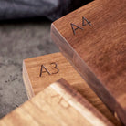 Drie Tareq Taylor Tarragon Snijplank Acacia A4 30/21 planken zijn gestapeld op een grijs oppervlak, elk gegraveerd in de hoek en accentueren de rijke acaciahoutnerf.