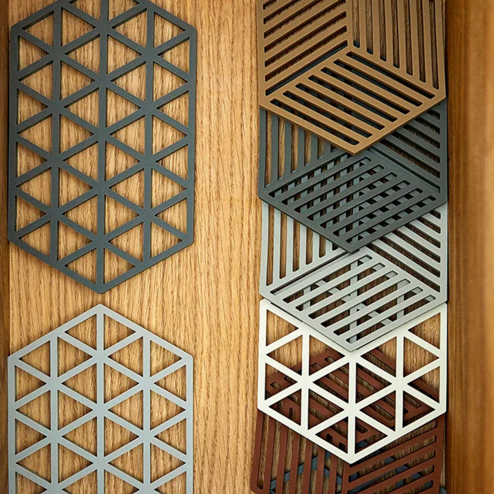 Zeshoekige metalen patronen met geometrische uitsparingen in driehoekige en gestreepte ontwerpen sieren de Zone Denmark Hexagon Trivet Olijfgroen-een stijlvolle olijfgroen onderzetter van Zone Denmark voor moderne tafelbladen.