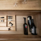Een houten lade in Scandinavische stijl herbergt de Zone Denmark Rocks Wijnopener & Wijn Stopper Gloss 2 st. Daarnaast staan er drie wijnflessen en twee omgekeerde glazen op het houten oppervlak.